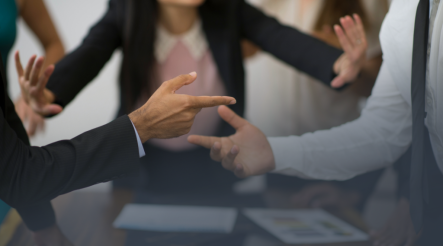 Partners wearing suits in dispute over the boardroom table, pointing fingers at one another