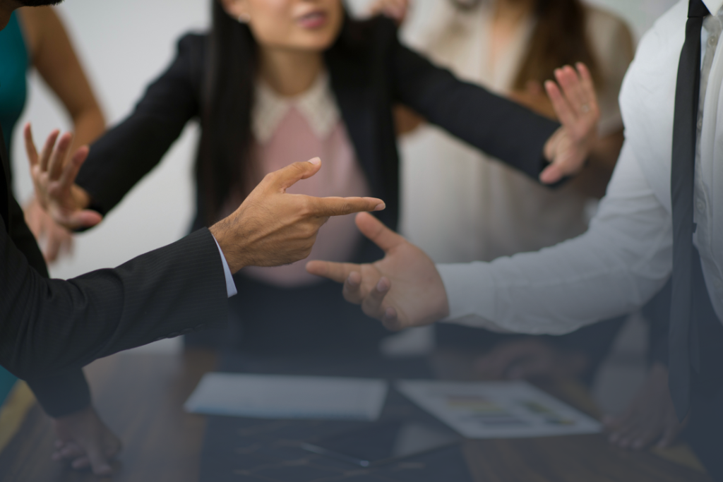 Partners wearing suits in dispute over the boardroom table, pointing fingers at one another